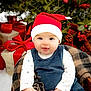 baby, child, santa_hat, holiday, christmas, smile, plaid_blanket, pinecones, berries, wrapped_gifts, festive, winter_clothing, cute, cheerful, indoors, portrait, seasonal, red, green, cozy