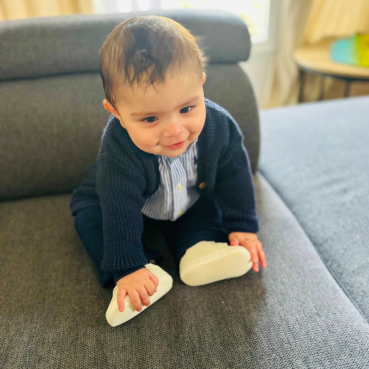 Youssef participe au concours pour gagner de l'argent avec cette photo : baby, child, toddler, couch, indoor, clothing, cardigan, white_shoes, curly_hair, cute, smiling, playful, furniture, window, natural_light, home, sitting, face, person, portrait