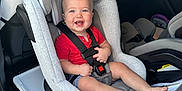 Leopold is registered to the contest to win money with this photo: baby, infant, child, car_seat, smiling, seatbelt, car_interior, vehicle, toddler, happy, barefoot, red_shirt, gray_upholstery, buckle, headrest, portrait, window, rearview_mirror, door, safety