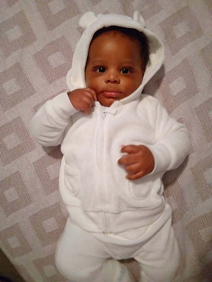 Xavion is registered to the contest to win money with this photo: arm, baby, baby_toddler_clothing, cheek, comfort, dress_shirt, eye, eyebrow, face, gesture, hand, head, linens, lip, nose, person, sleeve, smile, textile, thumb