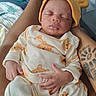baby, sleeping, infant, bear_outfit, yellow_hat, tattoo, arm, hand, cozy, soft_lighting, indoor, person, child, cute, peaceful, portrait, fabric, clothing, resting, newborn