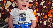 Adaline is registered to the contest to win money with this photo: baby, infant, child, smiling, laughing, portrait, indoors, blanket, colorful, bow, headband, white_shirt, blue_shorts, pepsi_logo, sitting, happy, face, person, text_on_clothing, cozy