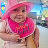 Adaline joined the competition — help win amazing prizes! baby, infant, child, portrait, smiling, happy, pink_hat, firefighter_hat, junior_firefighter, bib, clothing, held_by_adult, adult_arm, outdoor, amusement_park, sunlight, vehicle, table, close_up, family_photo