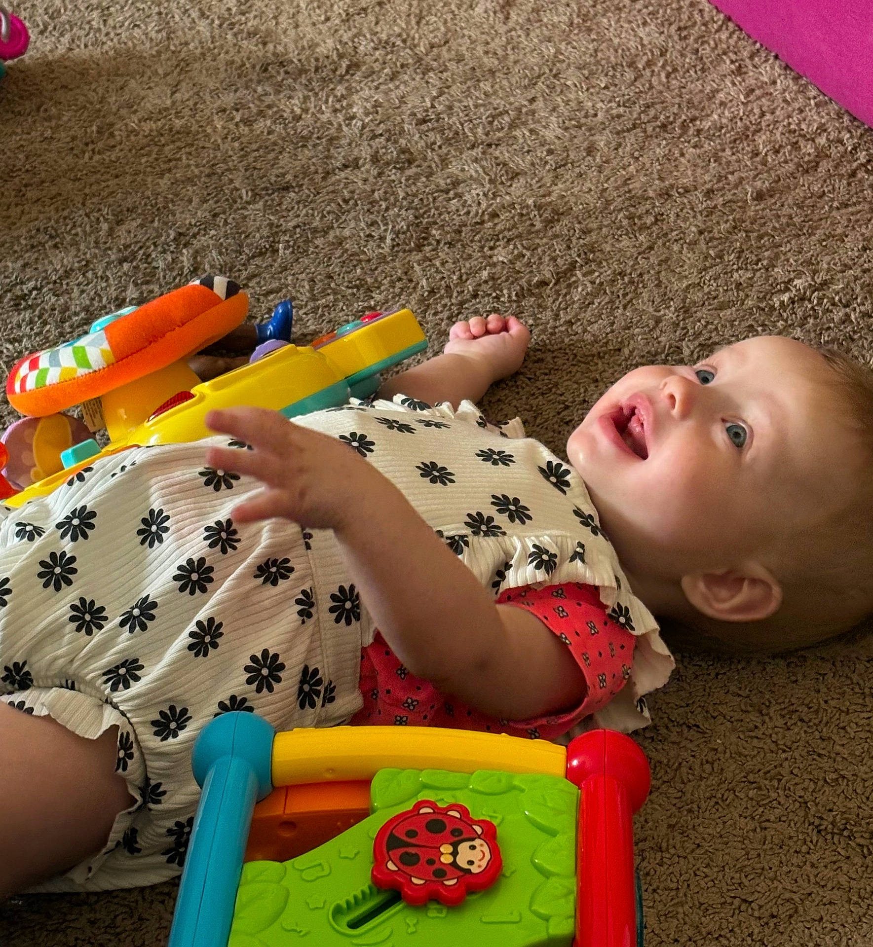 Emelia joined the competition — help win amazing prizes! baby, blue, bright_colors, carpet, child, colorful, cute, face, hand, happy, indoor, infant, lying_down, patterned_clothing, person, play, red, smiling, toy, yellow
