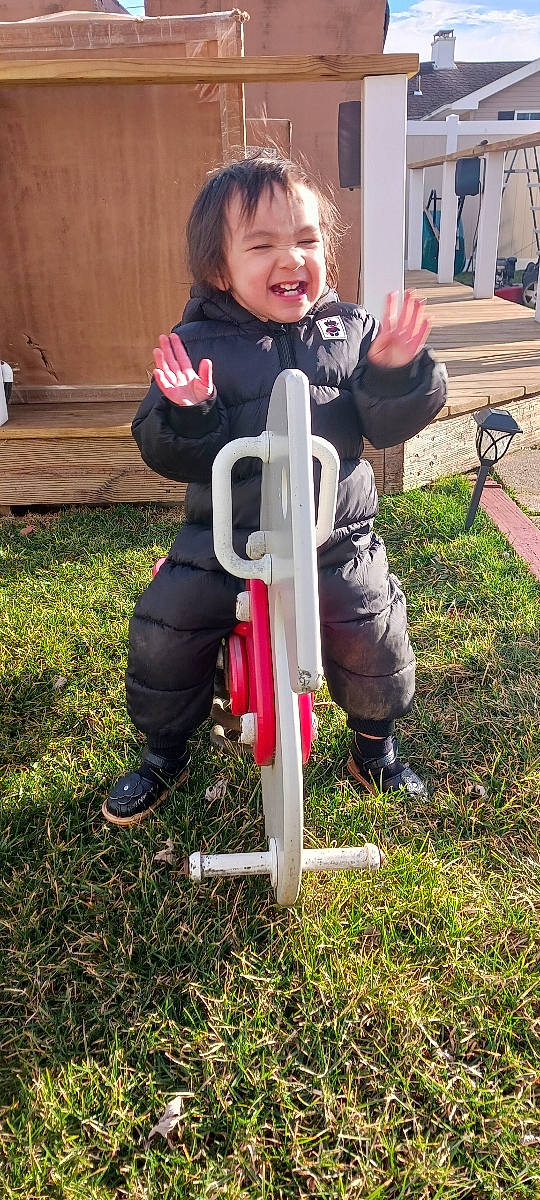 Ariana joined the competition — help win amazing prizes! baby_products, bicycle_accessory, bicycle_frame, bicycle_part, child, fun, grass, leisure, outdoor_play_equipment, person, personal_protective_equipment, plant, recreation, riding_toy, sitting, smile, sneakers, swing, tire, toddler