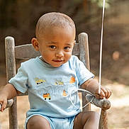 Samuel is registered to the contest to win money with this photo: toddler, child, baby, blue_clothing, wooden_chair, outdoor, balloon_string, smiling, curious, short_hair, sunlight, summer, cute, portrait, sitting, person, young_child, casual, daytime, nature_background