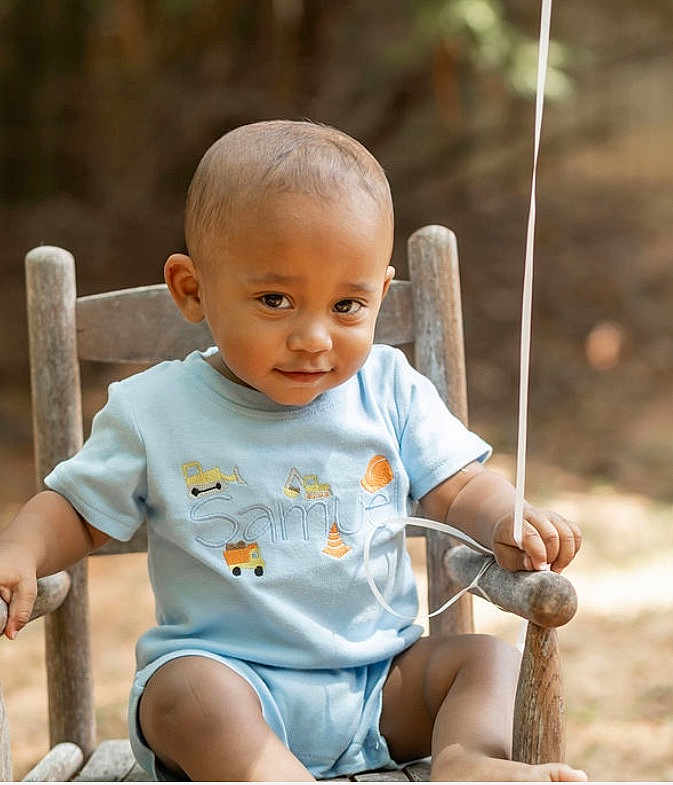 Samuel is registered to the contest to win money with this photo: toddler, child, baby, blue_clothing, wooden_chair, outdoor, balloon_string, smiling, curious, short_hair, sunlight, summer, cute, portrait, sitting, person, young_child, casual, daytime, nature_background