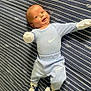 baby, infant, child, lying_down, blue_clothing, mittens, socks, bedspread, striped_pattern, smiling, happy, cute, portrait, indoor, person, young_child, head, face, apparel, soft_lighting