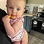 Lexley is registered to the contest to win money with this photo: baby, child, person, kitchen, food, snack, holding, arm, blue_eyes, face, messy, stove, towels, blender, cabinet, floor, countertop, tile_wall, clothing, indoor