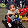 Jax is registered to the contest to win money with this photo: toddler, child, bike, balance_bike, strider, shoes, curly_hair, store, carpet, clothing, apparel, box, handlebars, toy, indoor, young_child, person, footwear, retail, curious