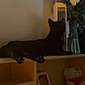 black_cat, cat, shelf, flowers, vase, teddy_bear, picture_frame, wooden_furniture, indoor, dim_lighting, pet, animal, feline, decor, cozy, resting, curious, home, soft_toys, relaxed