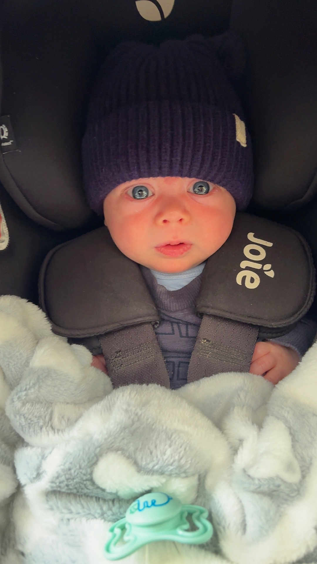 Archie is registered to the contest to win money with this photo: baby, infant, car_seat, hat, knit_hat, blanket, pacifier, child, blue_eyes, clothing, straps, closeup, face, cute, young_child, indoor, warm, soft_texture, person, portrait