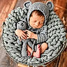 newborn, baby, knit_hat, bear_ears, crochet_toy, basket, chunky_knit_blanket, striped_clothing, sleeping, peaceful, wooden_floor, soft_lighting, infant, cozy, cute, toddler, hand_holding_toy, foot, portrait, indoors