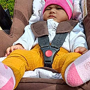 Farah a rejoint le concours — aidez-le/la à gagner de superbes lots ! baby, candid, child, clothing, daylight, expression, face, footwear, greenery, infant, nature, outdoor, person, pink_hat, portrait, seatbelt, sock, stone_building, stroller, yellow_pants