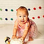 baby, child, cake, pink_dress, smiling, crawling, sprinkles, toy_penguin, messy, celebration, colorful, happy, indoor, white_floor, pom_poms, cute, portrait, food, birthday, playful