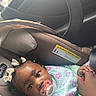 Kaylani is registered to the contest to win money with this photo: baby, car_seat, pacifier, child, infant, holding_hands, hair_bows, car_interior, seatbelt, cute, close_up, person, young_child, clothing, toddler, face, expression, sitting, parent, bonding
