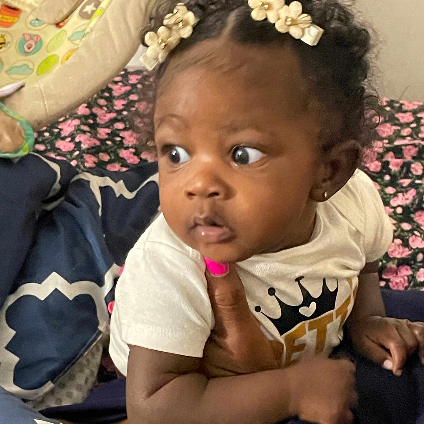 Kaylani joined the competition — help win amazing prizes! baby, child, curly_hair, hair_clips, hand, pink_nail_polish, white_shirt, face, looking_away, bed, blanket, winnie_the_pooh, baby_seat, earrings, indoor, person, cute, expression, holding, toddler