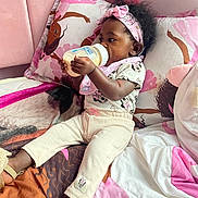 Kaylani is registered to the contest to win money with this photo: bed, blanket, bottle, cartoon, child, clothing, cozy, cute, drinking, headband, illustration, indoor, person, pillow, pink, sleepwear, slippers, soft, toddler, toy