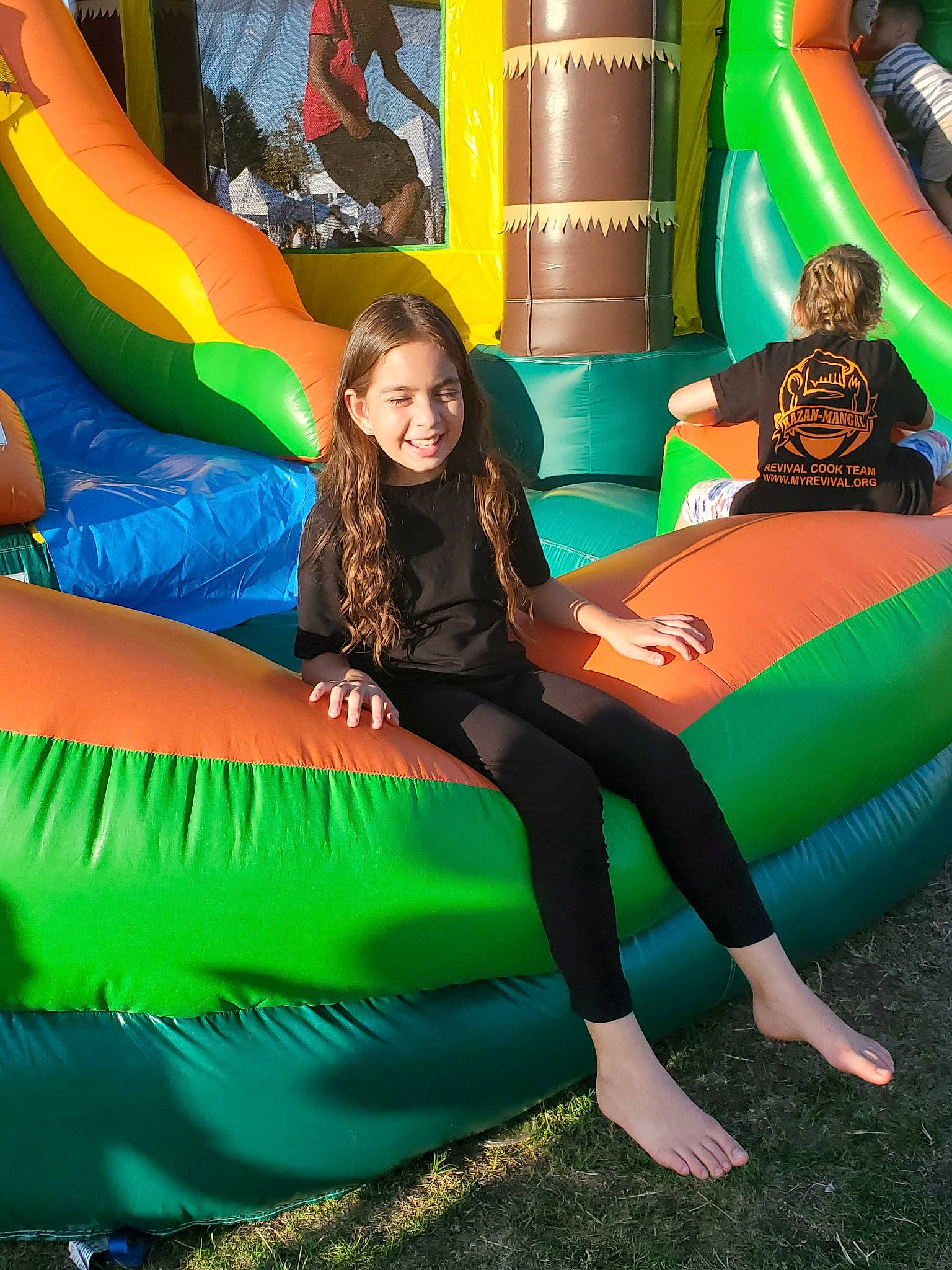 Cecilia is registered to the contest to win money with this photo: bounce_house, fun, games, green, inflatable, joy, leg, leisure, outdoor_play_equipment, person, recreation, sitting, smile, style