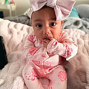 Leora is registered to the contest to win money with this photo: baby, child, pink_bow, headband, onesie, ladybug_pattern, blanket, soft_texture, indoor, cute, portrait, finger_in_mouth, sitting, infant, cozy, clothing, young_child, person, face, curious
