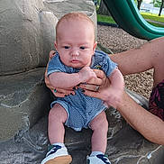 Allan is registered to the contest to win money with this photo: baby, infant, child, striped_clothing, blue_onesie, shoes, hands, adult, playground, slide, stone_surface, outdoor, park, grass, trees, daylight, skin, person, sitting, cute