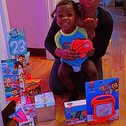 Chase joined the competition — help win amazing prizes! child, adult, basketball, toys, gifts, floor, indoor, wood_floor, smiling, person, black_hair, colorful, puzzle, snack, packaging, celebration, home, walls, doorway, happy