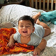 Atharv joined the competition — help win amazing prizes! baby, smiling, bed, blanket, crib, room, child, infant, happy, indoors, furniture, orange_cloth, person, sleepwear, wooden_crib, pillow, head, face, hand, foot