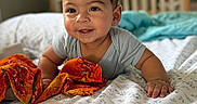 Atharv is registered to the contest to win money with this photo: baby, child, bed, blanket, crawling, orange_cloth, smiling, indoors, face, person, happy, young_child, head, hair, pajamas, comfort, room, light, home, portrait