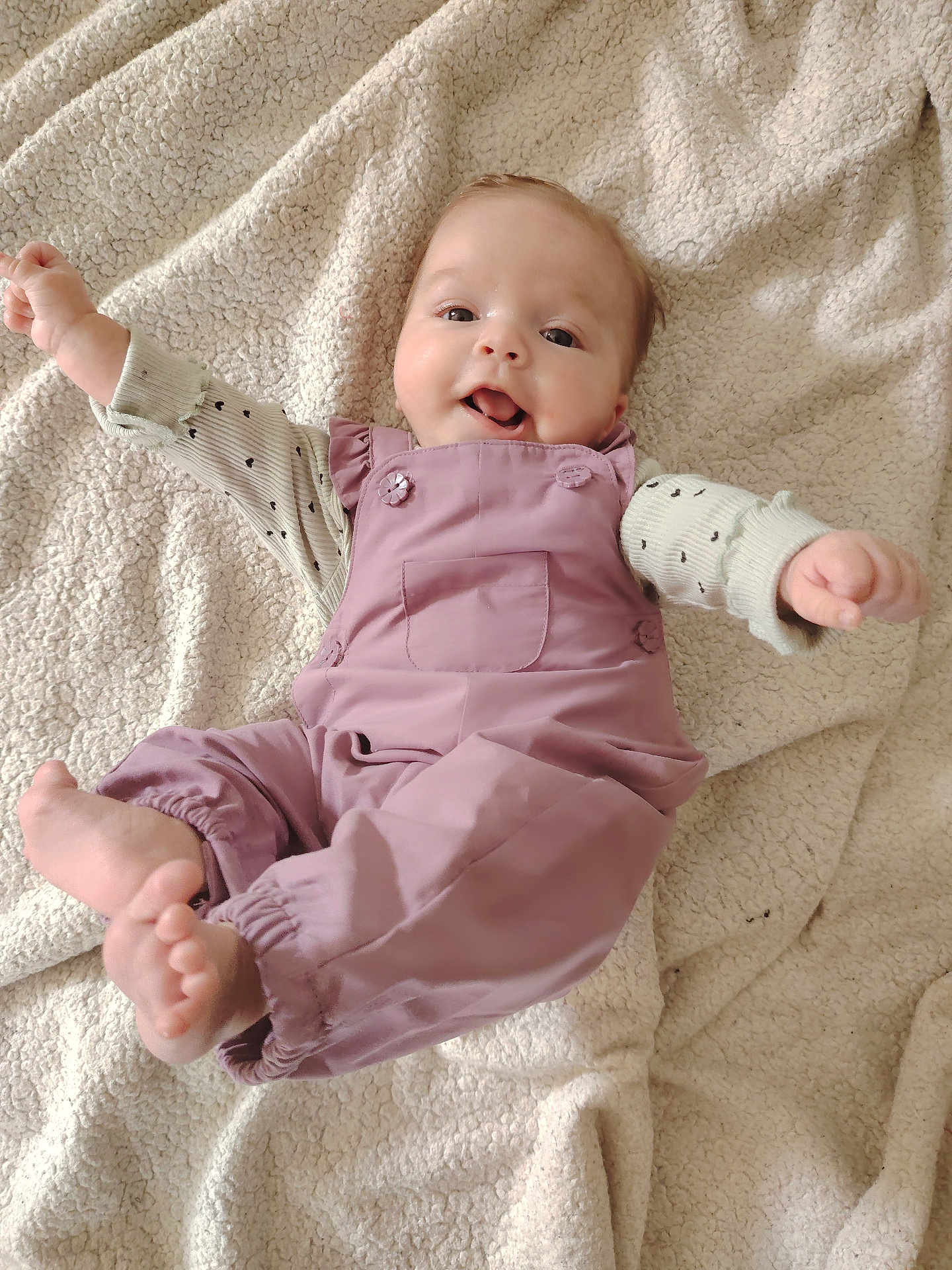 Camille participe au concours pour gagner de l'argent avec cette photo : baby, infant, smiling, romper, blanket, cute, happy, clothing, foot, hand, face, lying_down, soft_texture, child, playful, indoors, person, apparel, head, skin