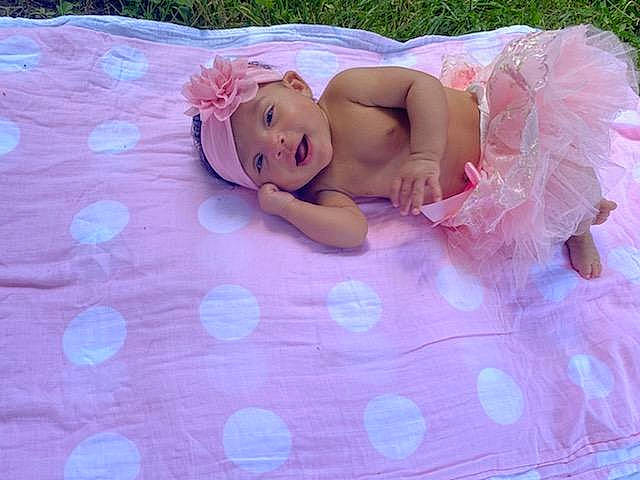 Kensleigh is registered to the contest to win money with this photo: arm, baby, baby_toddler_clothing, doll, dress, eye, fawn, grass, hair, happy, head, headwear, human_body, linens, person, petal, pink, purple, textile, toddler