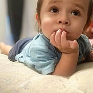 Leo is registered to the contest to win money with this photo: baby, child, infant, face, hand, expression, curious, indoor, mattress, clothing, blue_shirt, portrait, closeup, skin, head, eyes, young, resting, soft, background_blur