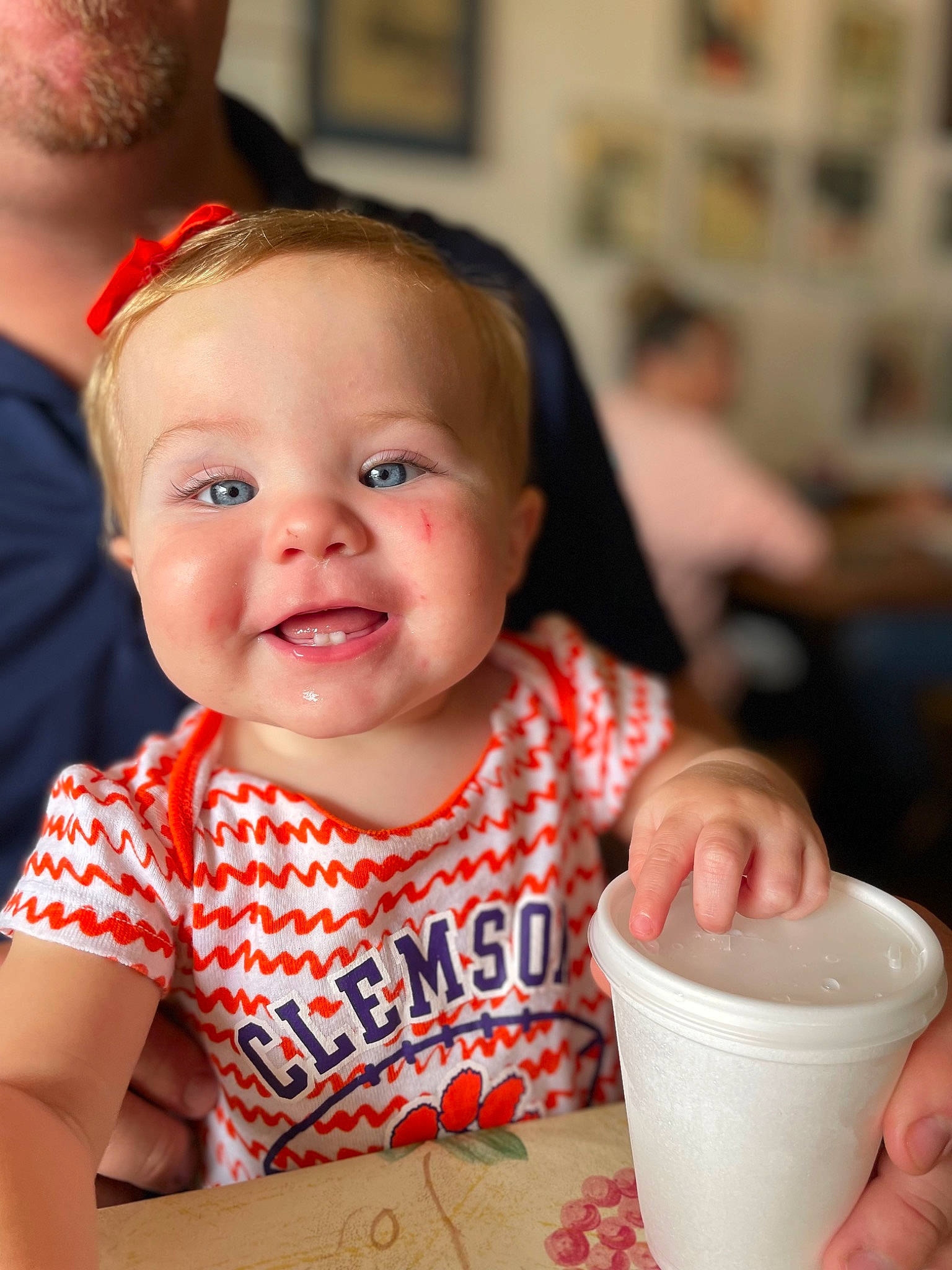Macie is registered to the contest to win money with this photo: baby, baby_toddler_clothing, chair, cheek, child, cup, drink, drinkware, event, fun, happy, joy, person, serveware, sitting, skin, sleeve, smile, t_shirt, table