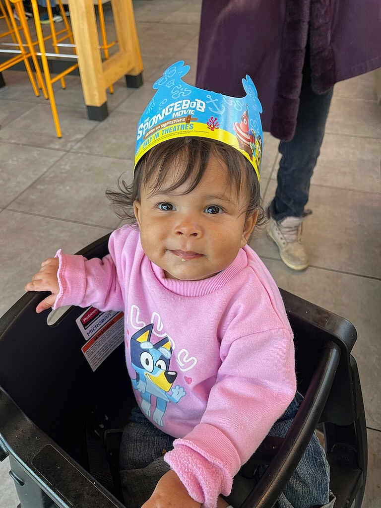 Jacquelyn joined the competition — help win amazing prizes! toddler, child, pink_sweatshirt, cartoon_character, spongebob, paper_crown, stroller, indoor, tile_floor, person, casual_shoes, curly_hair, cute, smiling, bluey, clothing, playful, young_child, portrait, seated