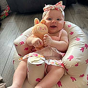 Darcie-Rae joined the competition — help win amazing prizes! baby, infant, child, plush_toy, pink, headband, smiling, sitting, indoor, flooring, inflatable_chair, bunny_pattern, cute, happy, toy, dress, footwear_free, living_room, soft_lighting, playful