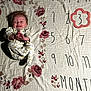 baby, infant, smiling, milestone_blanket, floral_pattern, numbers, months, clapping, happy, lying_down, white_clothing, pink_flowers, cute, young_child, portrait, indoor, celebration, head, hands, face