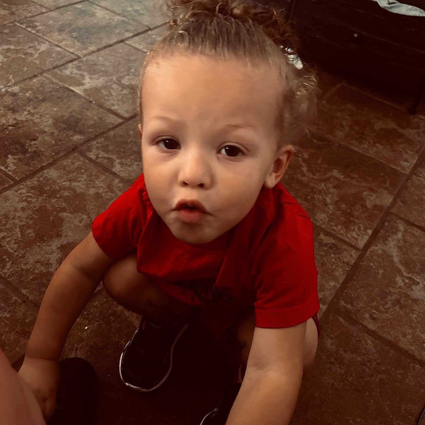 Legend joined the competition — help win amazing prizes! child, toddler, curly_hair, red_shirt, sneakers, floor, tile_floor, indoor, expression, reaching_out, person, young_child, hair_tied, crouching, cute, curious, brown_eyes, casual_clothing, skin, portrait