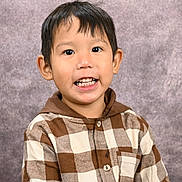 Lucius is registered to the contest to win money with this photo: boy, brown_hair, buttoned_shirt, casual_clothing, checkered_shirt, child, cute, expression, face, happy, head_and_shoulders, hoodie, indoor, light_skin, person, portrait, smiling, studio_background, teeth, young