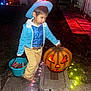 child, boy, costume, cowboy, hat, jack_o_lantern, pumpkin, candy, bucket, halloween, night, outdoor, decorations, lights, sidewalk, pants, shirt, jacket, belt, holiday