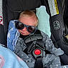 baby, car_seat, sunglasses, blanket, infant, clothing, straps, seatbelt, star_pattern, cute, sleeping, child, indoors, comfort, headwear, resting, closeup, infant_clothing, baby_accessory, soft_toys