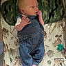 baby, denim_overalls, infant, blanket, pattern, camouflage_pillow, face, hand, foot, lying_down, bed, soft_toys, child, clothing, newborn, cute, indoors, resting, skin, person
