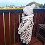 black_shoes, child, clouds, coat, deck, fence, footwear, girl, greenery, hat, leopard_print, mountain, nature, outdoor, profile, scarf, sky, standing, winter_clothing, wood