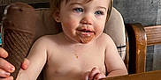Phenix is registered to the contest to win money with this photo: toddler, child, ice_cream, chocolate, high_chair, messy_face, shirtless, wooden_table, wooden_wall, indoor, curious_expression, holding, food, snack, young_child, person, cute, mess, brown_hair, blue_eyes