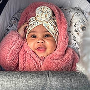 Alani-Rae is registered to the contest to win money with this photo: baby, child, smiling, headwrap, pink_jacket, stroller, pillow, bird_pattern, cozy, indoor, portrait, cute, happy, infant, face, clothing, fabric, warm, closeup, person