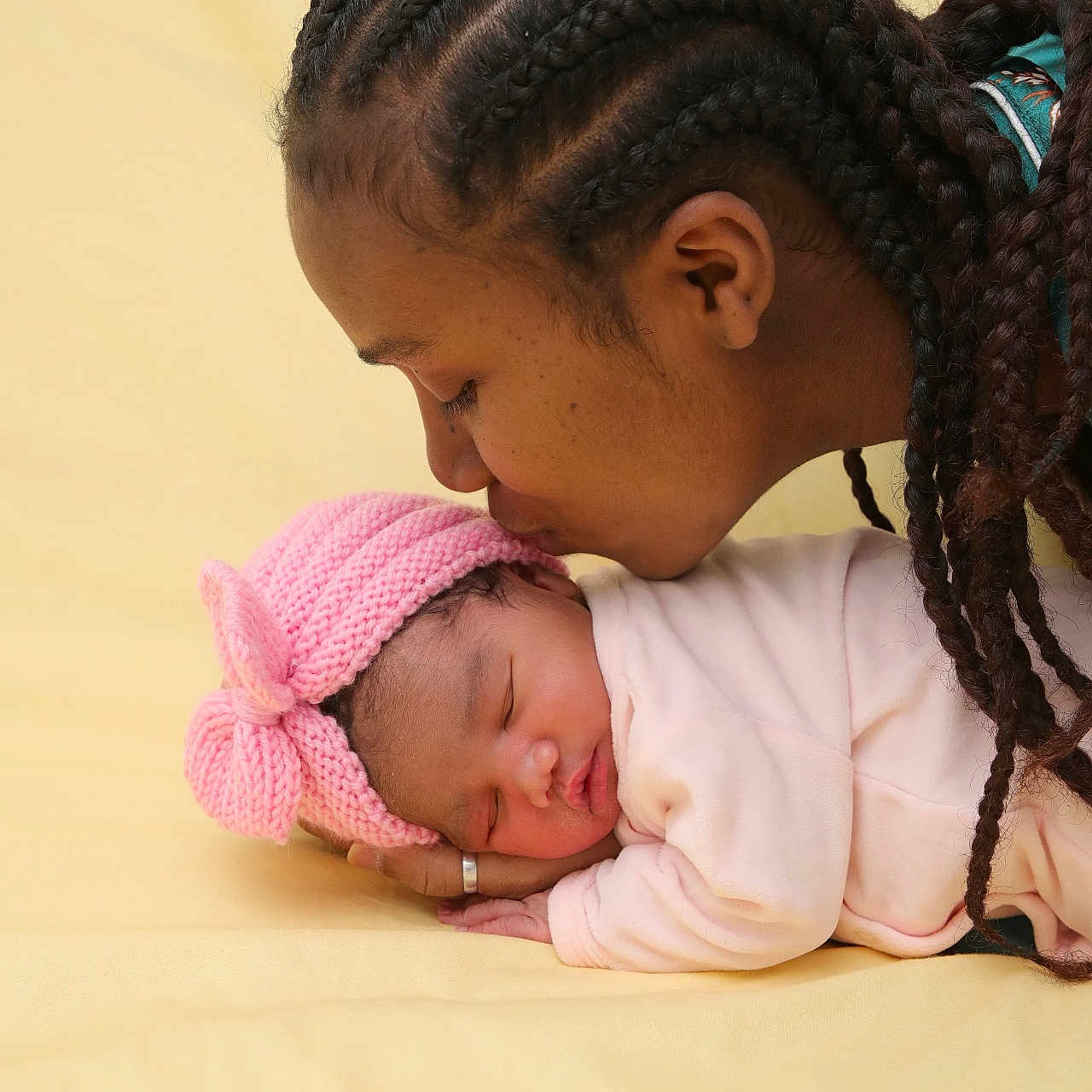 Nely a rejoint le concours — aidez-le/la à gagner de superbes lots ! adult, affection, baby, braids, close_up, family_moment, hand, infant, kiss, knit_hat, newborn, peaceful, pink_hat, portrait, ring, sleeping, soft_lighting, studio_background, swaddle, yellow_background