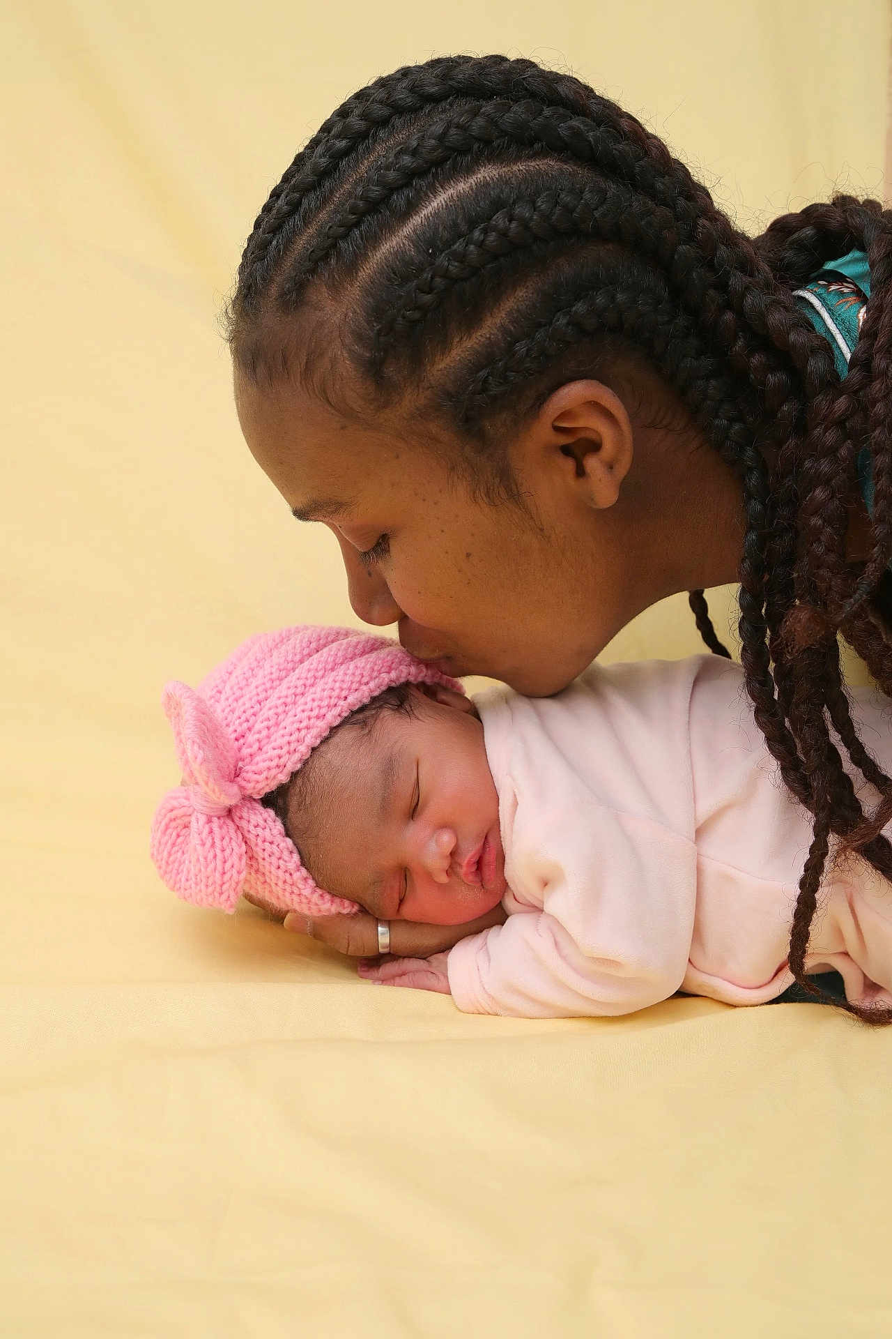 Nely a rejoint le concours — aidez-le/la à gagner de superbes lots ! adult, affection, baby, braids, close_up, family_moment, hand, infant, kiss, knit_hat, newborn, peaceful, pink_hat, portrait, ring, sleeping, soft_lighting, studio_background, swaddle, yellow_background