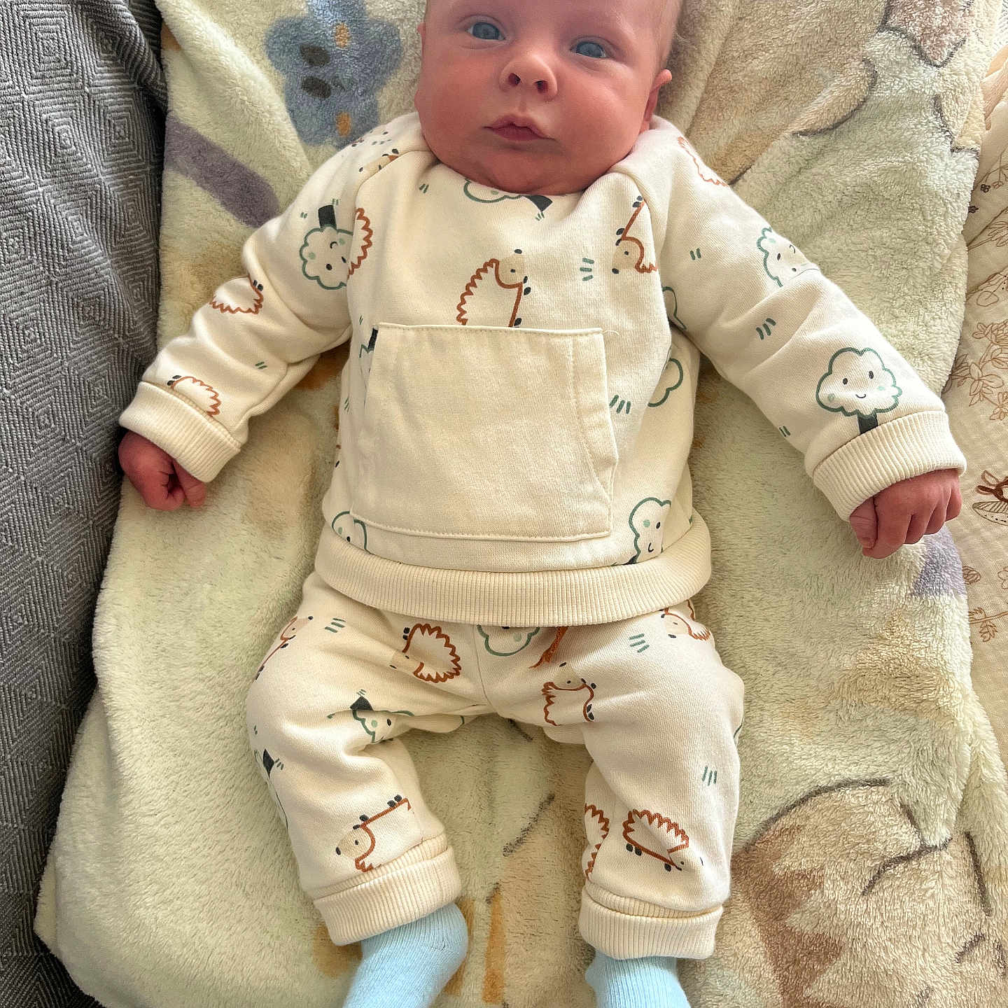 Louys a rejoint le concours — aidez-le/la à gagner de superbes lots ! baby, blanket, child, clothing, comfortable, cozy, cute, hedgehog_print, indoor, infant, lying_down, onesie, patterned, portrait, small_hands, socks, soft_texture, tree_print, warm_colors, wide_eyes