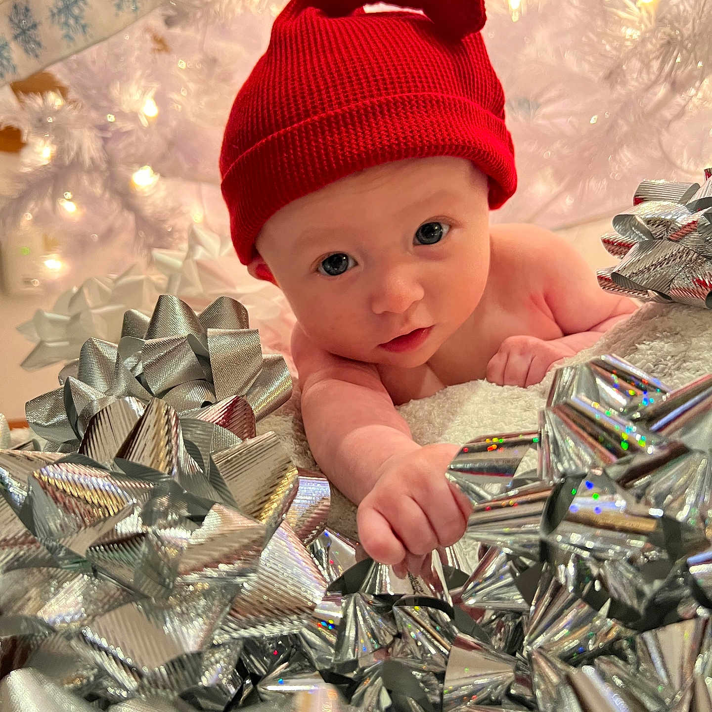 Carson is registered to the contest to win money with this photo: baby, celebration, child, christmas, closeup, curious, cute, decor, festive, holiday_lights, holiday_theme, indoor, infant, portrait, red_hat, seasonal, silver_bows, snowflake_decoration, soft_lighting, wrapped_gifts