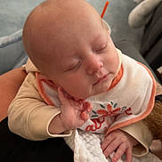 Carson is registered to the contest to win money with this photo: baby, sleeping, infant, blanket, bib, hand, face, cozy, indoor, person, cute, resting, soft, nursing_pillow, wood_floor, carpet, toy, clothing, closeup, peaceful