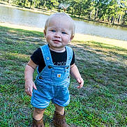 Paisley joined the competition — help win amazing prizes! toddler, child, grass, lake, water, trees, outdoor, nature, blue_overalls, boots, shorts, black_shirt, baby, sunlight, daytime, smiling, portrait, grass_field, cute, standing