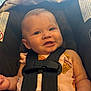 baby, child, car_seat, infant, smiling, happy, pink_clothing, ice_cream_pattern, safety_harness, seat_belt, cute, portrait, indoors, person, young_child, face, head, skin, hand, child_seat